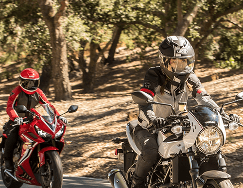 Two people riding motorcycles near a wooded area 